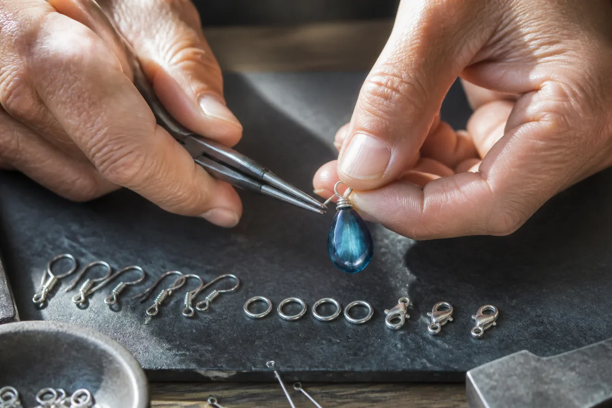 Mains d’artisan montant un pendentif de verre bleu sur un crochet en argent